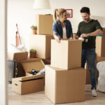 Couple packing stuff among plenty of cardboard boxes